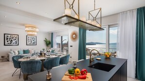 Una cocina moderna con una isla central, zona de comedor con sillas azules y vista al mar.