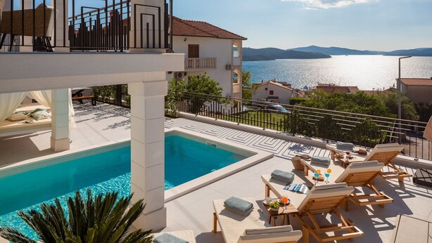 Zona de piscina con sillones de descanso y vista al mar.