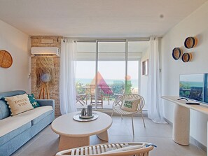 A modern living room with a sofa, a round table, a TV, and a balcony with a view of the sea. - Studio with Pool in Saint-Martin (Saint-Martin)