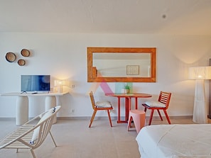 A hotel room with a bed, a desk with a TV, a table with chairs, and a mirror on the wall. - Studio with Pool in Saint-Martin (Saint-Martin)
