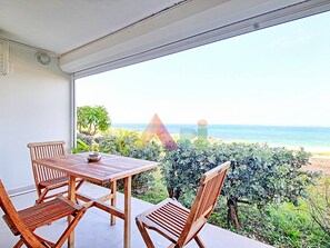 A balcony with a wooden table and chairs, overlooking a beach and ocean.