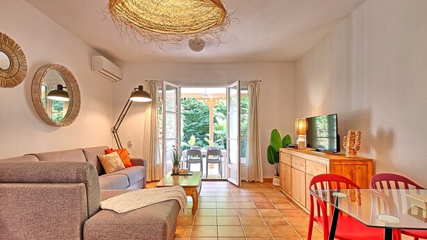 Een moderne woonkamer met een bank, een eettafel met stoelen, een televisie en een groot raam met gordijnen.