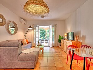 A modern living room with a sofa, a dining table with chairs, a TV, and a large window with curtains. - Villa Coquelicot - 2 Bedrooms, Beach and Garden (Saint-Martin)