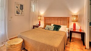Een slaapkamer met een houten hoofdbord, twee nachtkastjes met lampen, een geweven sprei en een geweven mand.