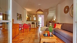 Een ruime woonkamer met een bank, rode stoelen, een houten salontafel en een keuken op de achtergrond.