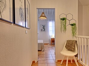 A hallway with a white chair, a hanging plant, and framed artwork on the wall. - Villa Coquelicot - 2 Bedrooms, Beach and Garden (Saint-Martin)