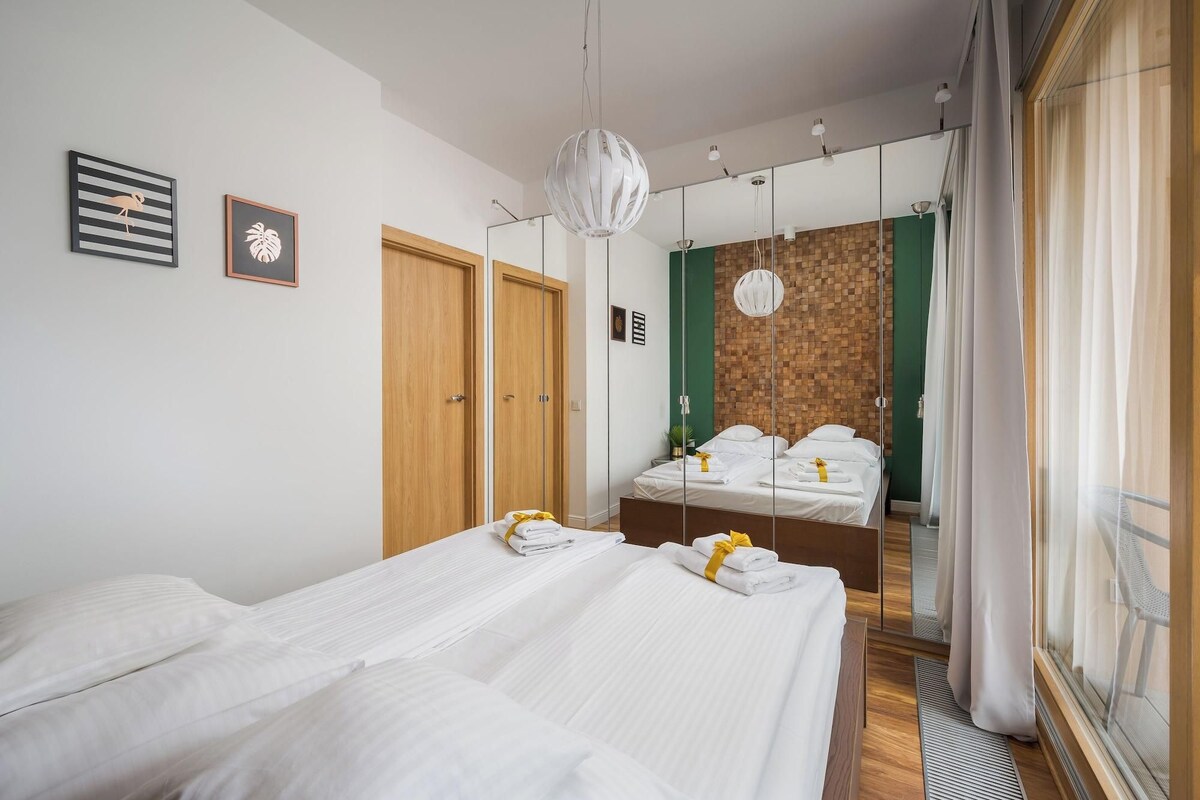 A hotel room with two beds, a wooden wardrobe, a mirror, and a green accent wall.