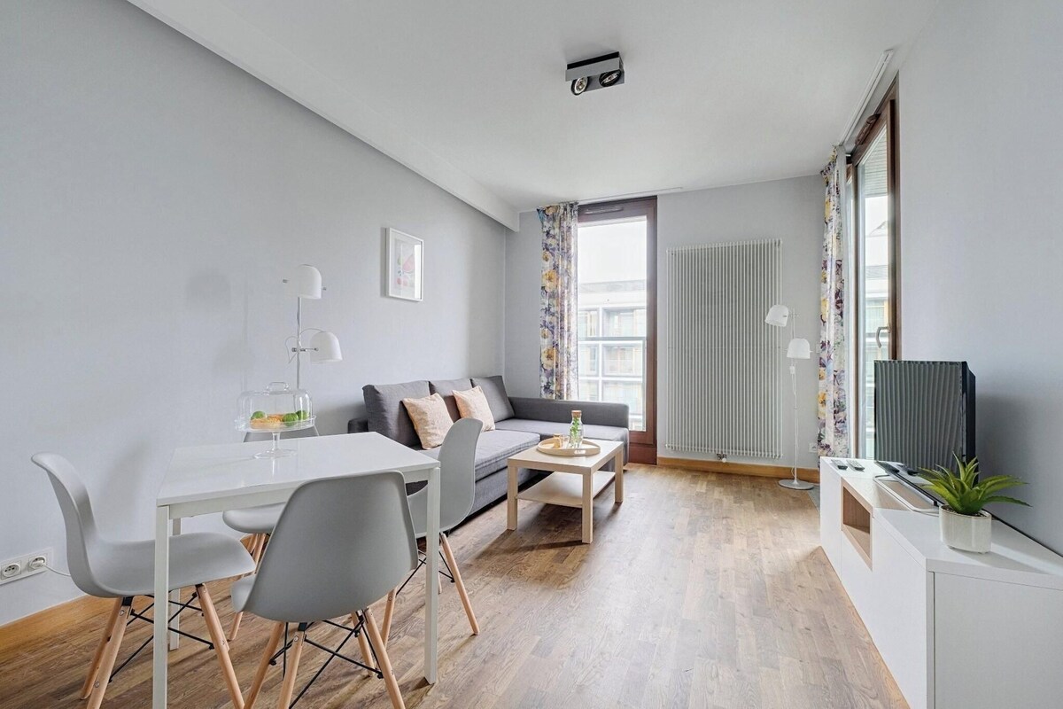 A modern living room with a sofa, dining table, chairs, a TV, and a radiator.