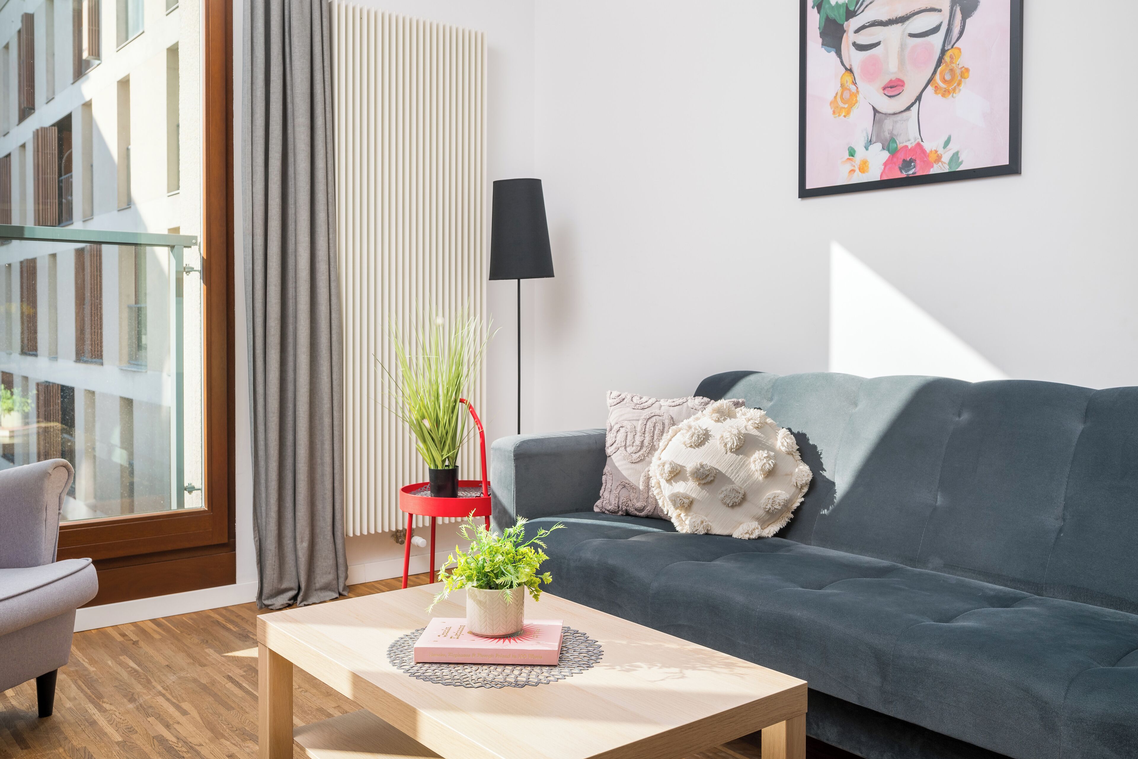 A modern living room with a grey sofa, a coffee table with a plant, a red chair, and a large window with curtains.