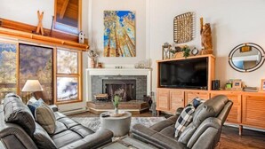 A cozy living room with a fireplace, leather sofas, a TV, and a large window. - Remodeled and Oversized 2-bedroom Condo in West Keystone With Mountain Views, Pool, hot tub & Shuttle to Slopes! (Keystone)