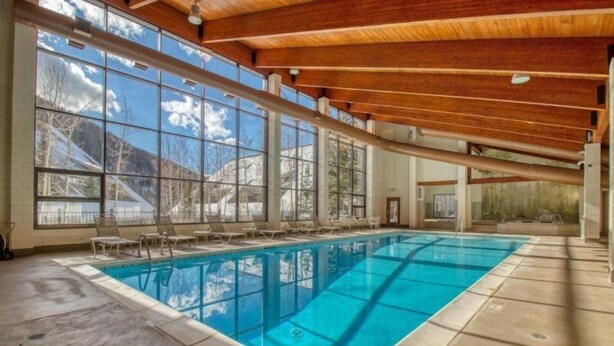 An indoor swimming pool with clear windows, wooden beams, and a view of mountains. - Remodeled and Oversized 2-bedroom Condo in West Keystone With Mountain Views, Pool, hot tub & Shuttle to Slopes! (Keystone)