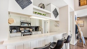 A modern kitchen with white cabinets, a central island with bar stools, and decorative wall art. - Remodeled and Oversized 2-bedroom Condo in West Keystone With Mountain Views, Pool, hot tub & Shuttle to Slopes! (Keystone)