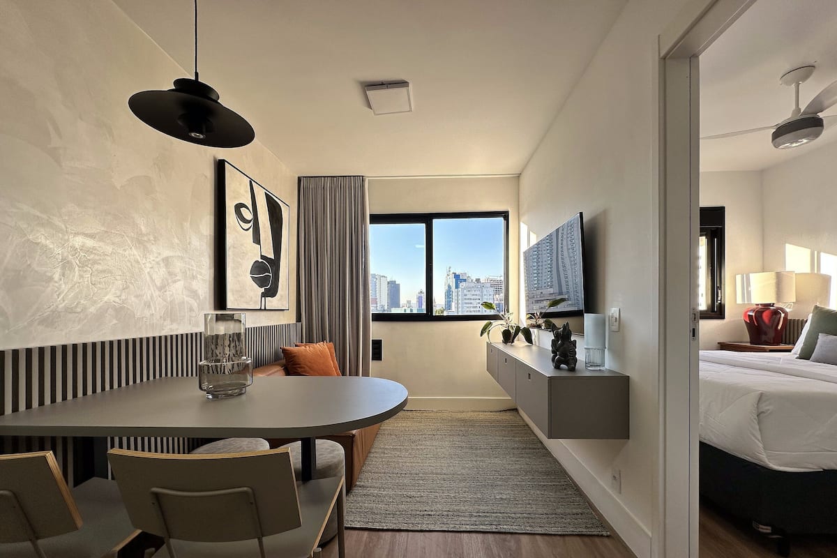A modern hotel room with a dining area, a bed, a TV, and a city view.