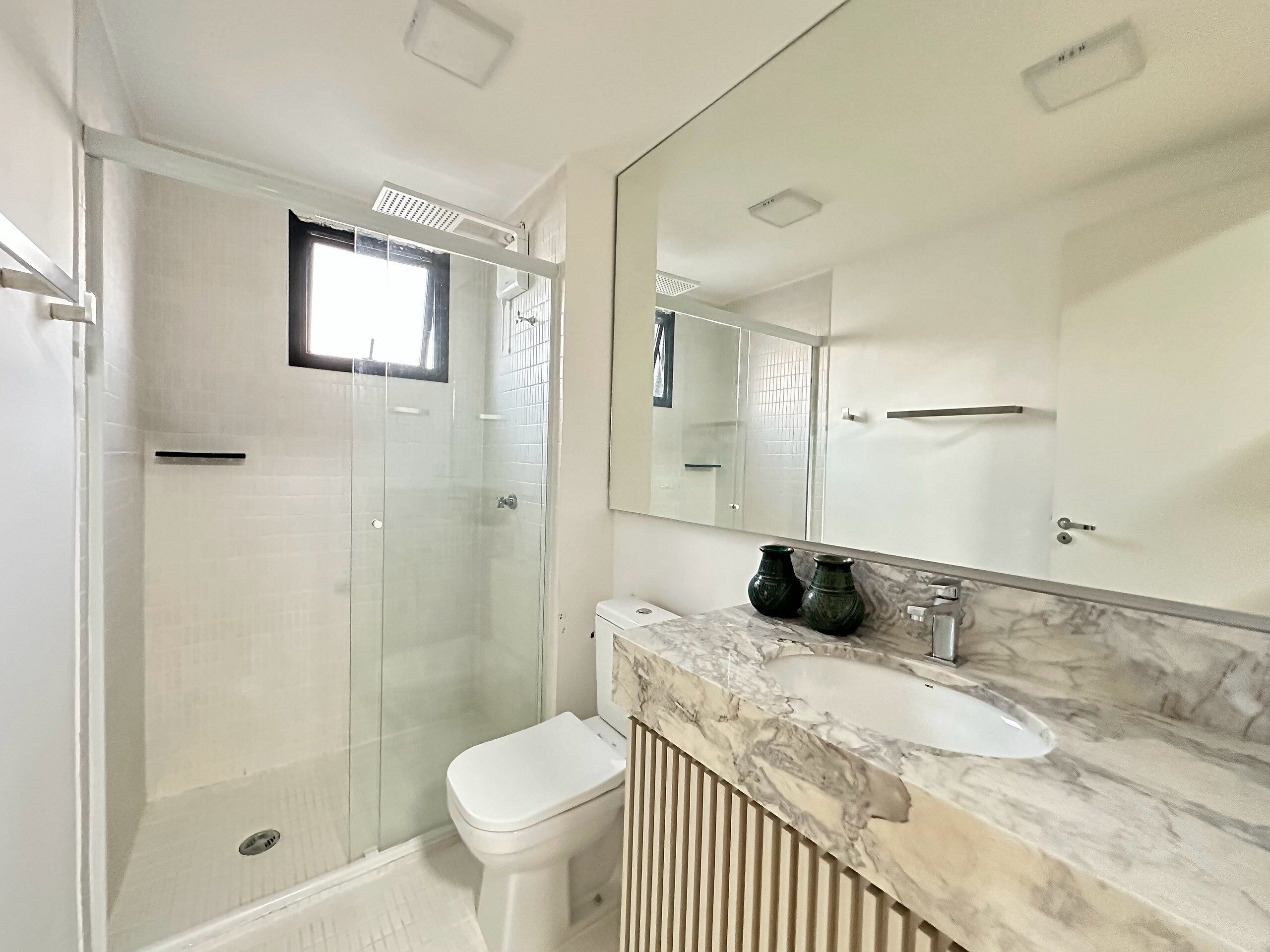 A modern bathroom with a glass-enclosed shower, a white toilet, a marble sink, and a large mirror.