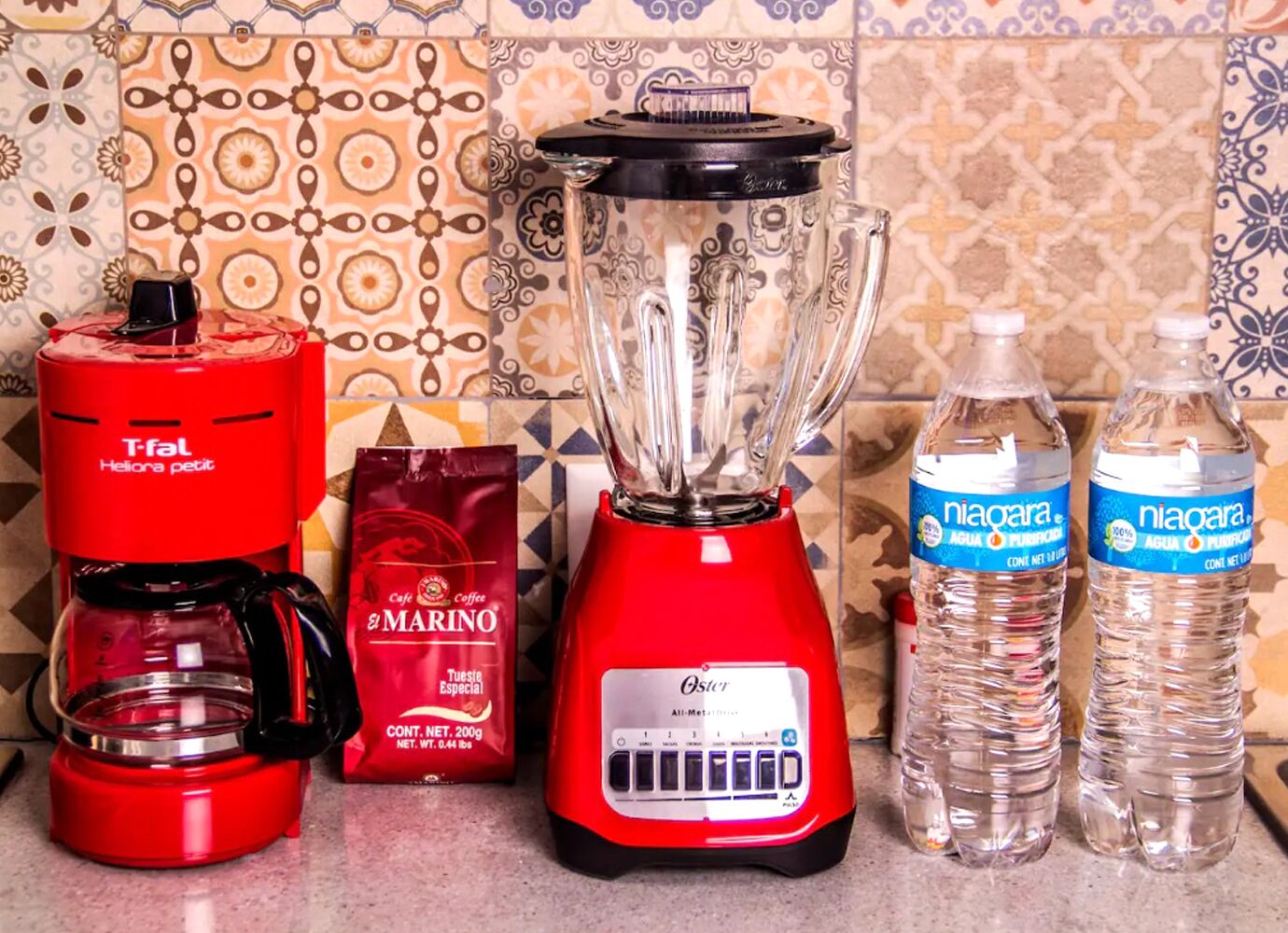 A kitchen counter with a red coffee maker, a blender, a coffee bag, and two water bottles.