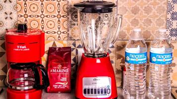 A kitchen counter with a red coffee maker, a blender, a coffee bag, and two water bottles.