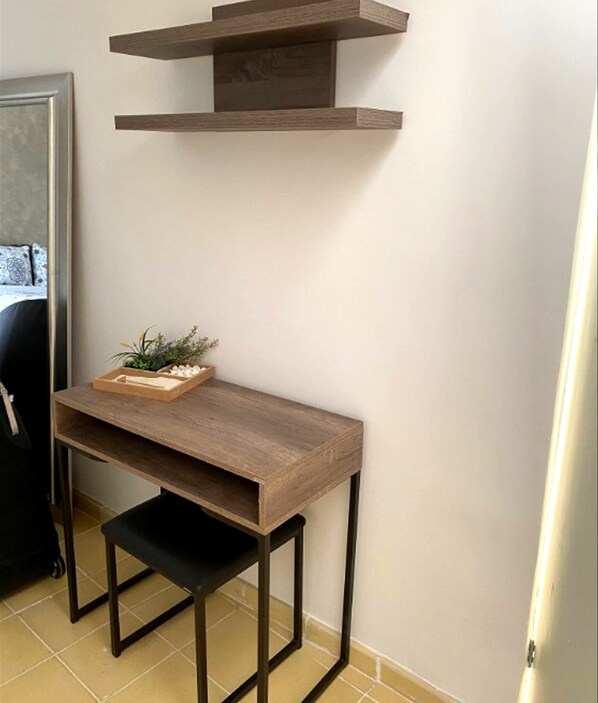 A small wooden desk with a black bench, a wooden tray with plants, and a wall-mounted shelf above.