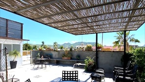 An outdoor patio area with a round glass table and four chairs, surrounded by potted plants and a bamboo pergola. - Villa Esterito (La Paz)