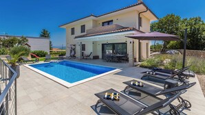 Une maison à deux étages dotée d’une piscine, d’un espace extérieur aménagé pour se détendre et d’un patio couvert.
