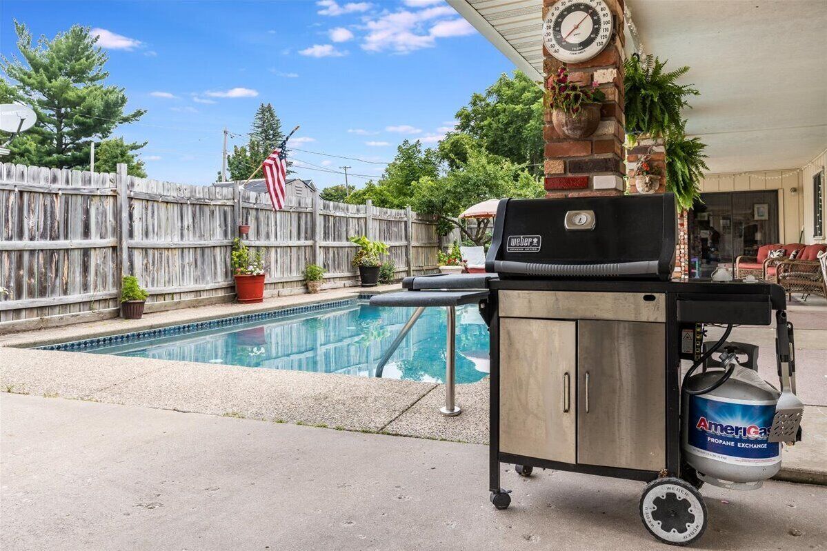 A poolside area with a grill, propane tank, and a clock on a brick wall.