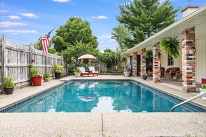 Enjoy a refreshing dip in the backyard pool surrounded by lush greenery and a fence.