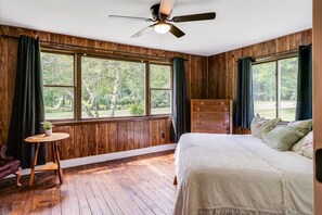 Traditional room with a view of lush green surroundings, featuring a bed, dresser, and small table with a plant.