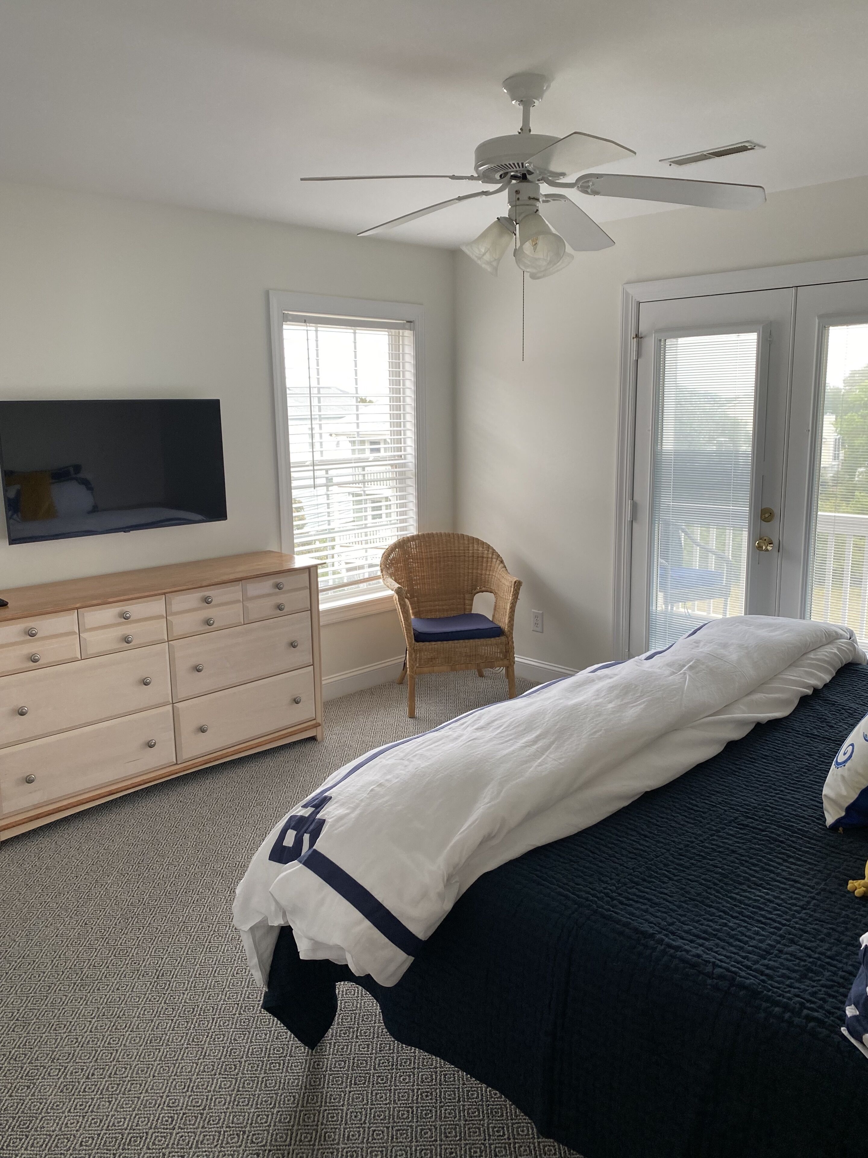 A bedroom with a bed, dresser, chair, ceiling fan, and a TV mounted on the wall.