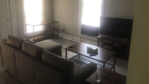 A living room with a sofa, a coffee table, a TV, and two windows with blinds. - Nice little hideaway close to all the downtown amenities  (Fort Wayne)