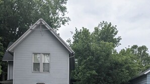 A two-story house with a front porch and a small garden area. - Nice little hideaway close to all the downtown amenities  (Fort Wayne)