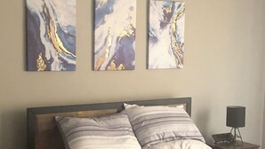 A bedroom with a bed, a nightstand, and three abstract paintings on the wall. - Nice little hideaway close to all the downtown amenities  (Fort Wayne)