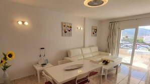 A modern dining area with a white table and chairs, a sofa, and artwork on the walls. - San Marino 5 (Los Cristianos)