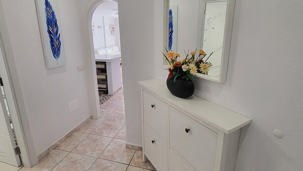 A hallway with a white cabinet, a mirror, and a vase with flowers. - San Marino 5 (Los Cristianos)
