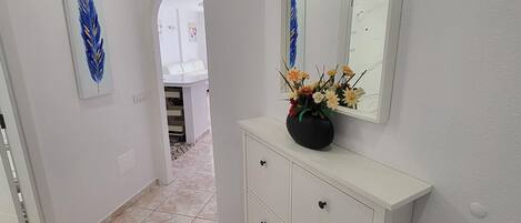 A hallway with a white cabinet, a mirror, and a vase with flowers.
