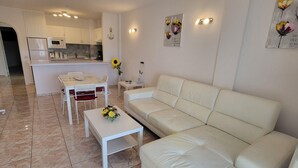 A modern living room with a white leather sofa, a small white coffee table, and a dining area with a white table and chairs. - San Marino 5 (Los Cristianos)