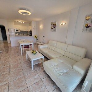 A modern living room with a white leather sofa, a small white coffee table, and a dining area with a white table and chairs. - San Marino 5 (Los Cristianos)