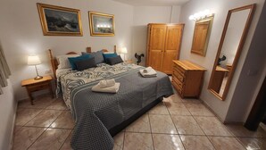 A bedroom with a bed, a wooden wardrobe, a bedside table with a lamp, a dresser, and a large mirror. - San Marino 5 (Los Cristianos)