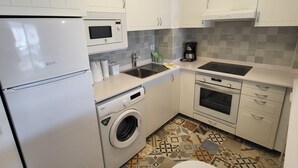 A compact kitchen with white cabinets, a microwave, a coffee maker, a washing machine, and a stove. - San Marino 5 (Los Cristianos)