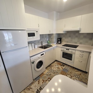 Une cuisine compacte avec des meubles blancs, un four à micro-ondes, une machine à café, un lave-linge et une cuisinière.