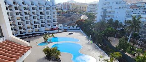 A hotel with a swimming pool, multiple balconies, and a view of surrounding buildings and hills.