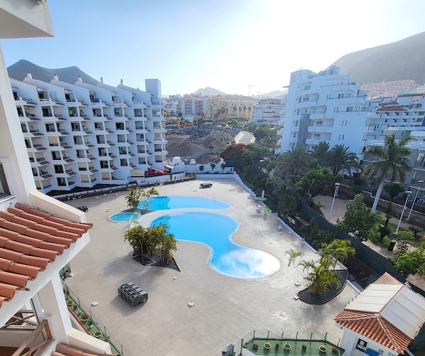Un hôtel doté d’une piscine, de plusieurs balcons et offrant une vue sur les bâtiments et les collines environnants.