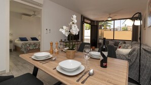 A dining area with a wooden table set for two, a bottle of wine, and white flowers.