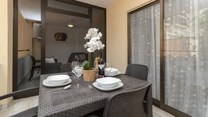 A dining area with a table set for two, a wicker chair, a wicker sofa, a white orchid, and a bottle of wine.