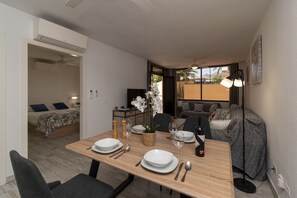 En spiseplads med et træbord dækket til to personer, en sofa, en gulvlampe og en seng i baggrunden.