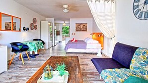 A modern living room with a sofa, a coffee table with plants, a bed with a headboard, and a large wall clock. - Comfortable Studio with Pool and Wi-Fi Near Beach (Saint-Martin)