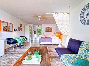 A modern living room with a sofa, a coffee table with plants, a bed with a headboard, and a large wall clock.