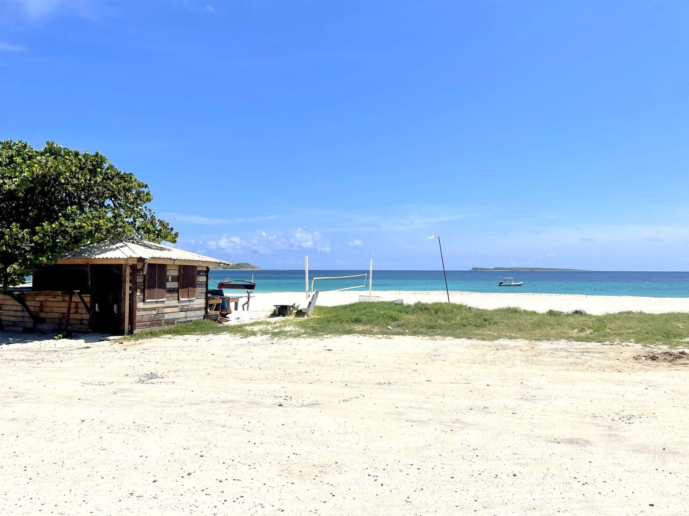 A beach with a small wooden structure, a volleyball net, and a clear view of the ocean.