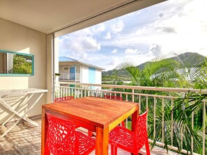 Un balcone con un tavolo di legno e sedie rosse, vista su una zona residenziale con case e palme.