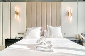A hotel room with a large bed, two bedside tables, a nightstand, and a wall-mounted light fixture.