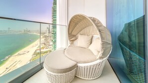 A balcony with a wicker chair and cushions, overlooking a beach and cityscape. - Picturesque Balcony and Beach Haven at Address JBR (Dubai)