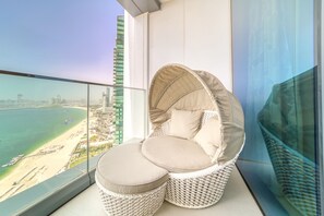 A balcony with a wicker chair and cushions, overlooking a beach and cityscape. - Picturesque Balcony and Beach Haven at Address JBR (Dubai)